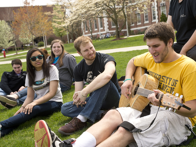 Students sitting in quad playing guitar