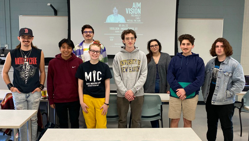 Eight students posing together for a photo in a classroom.