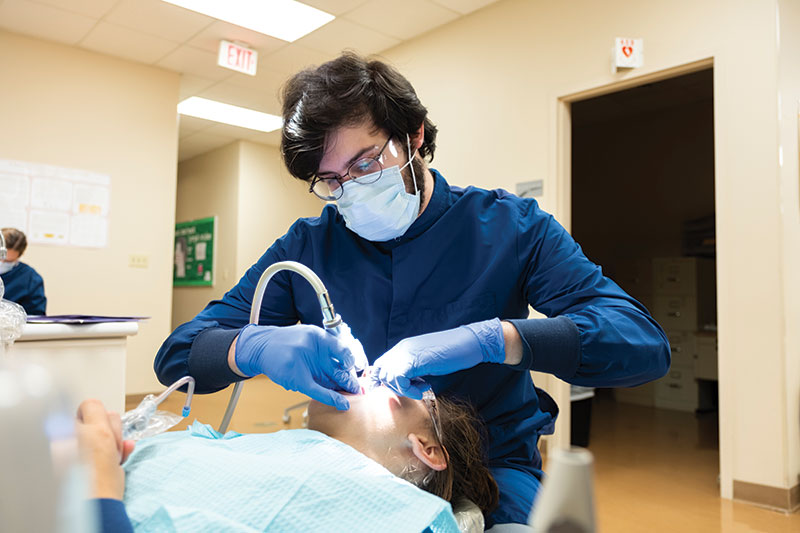 A dental hygiene student works on someone's teeth.