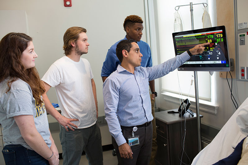 A faculty member points out something on a patient monitor.