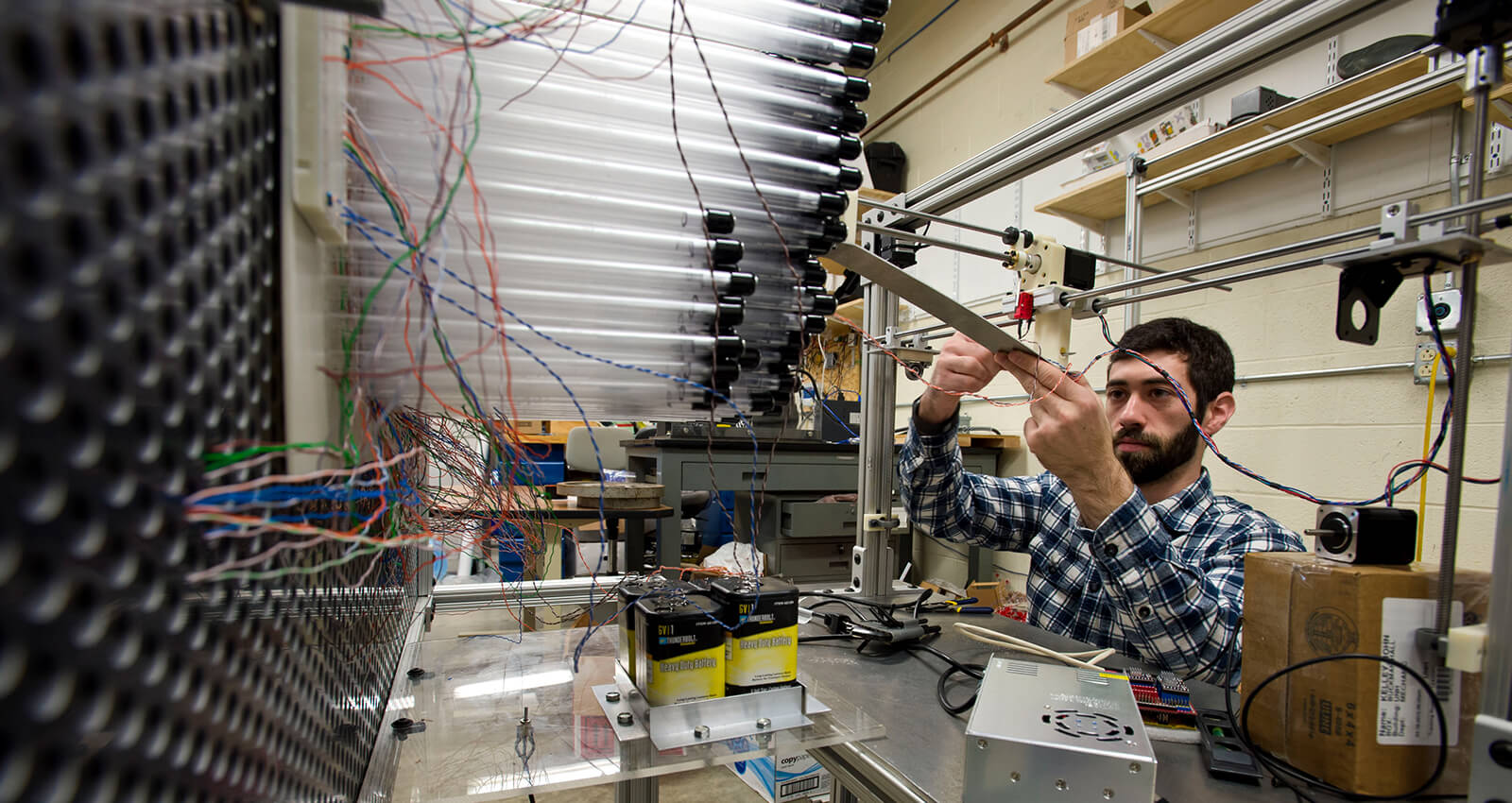 A student working on electrical wiring and circuit components in an engineering laboratory.