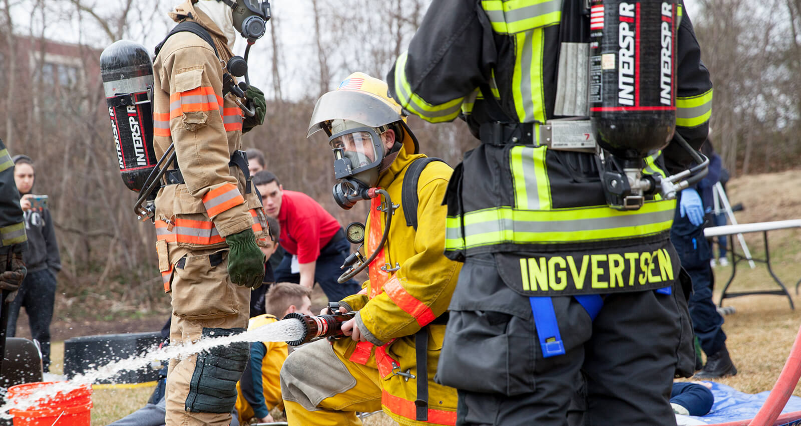Student in firefighter gear using fire hose