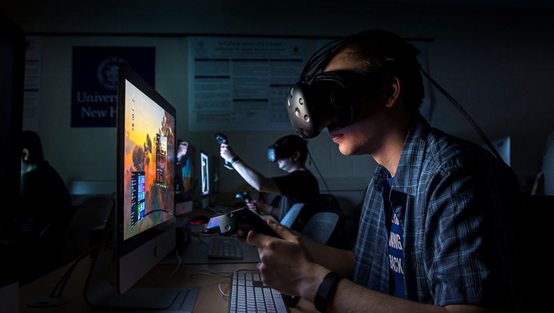 A student, wearing a virtual headset, interacts with a computer monitor.