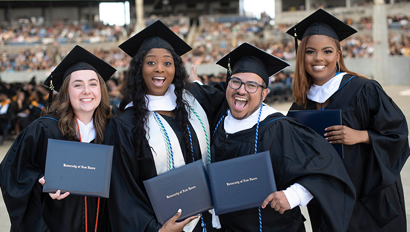 Four graduates, in cap and gown, pose for a photo.