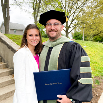 Aaron S. Marks ’24 DHSc with is wife, Nicole. She/U+0026#x27;s wearing white and he/U+0026#x27;s in his cap and gown, holding his diploma.