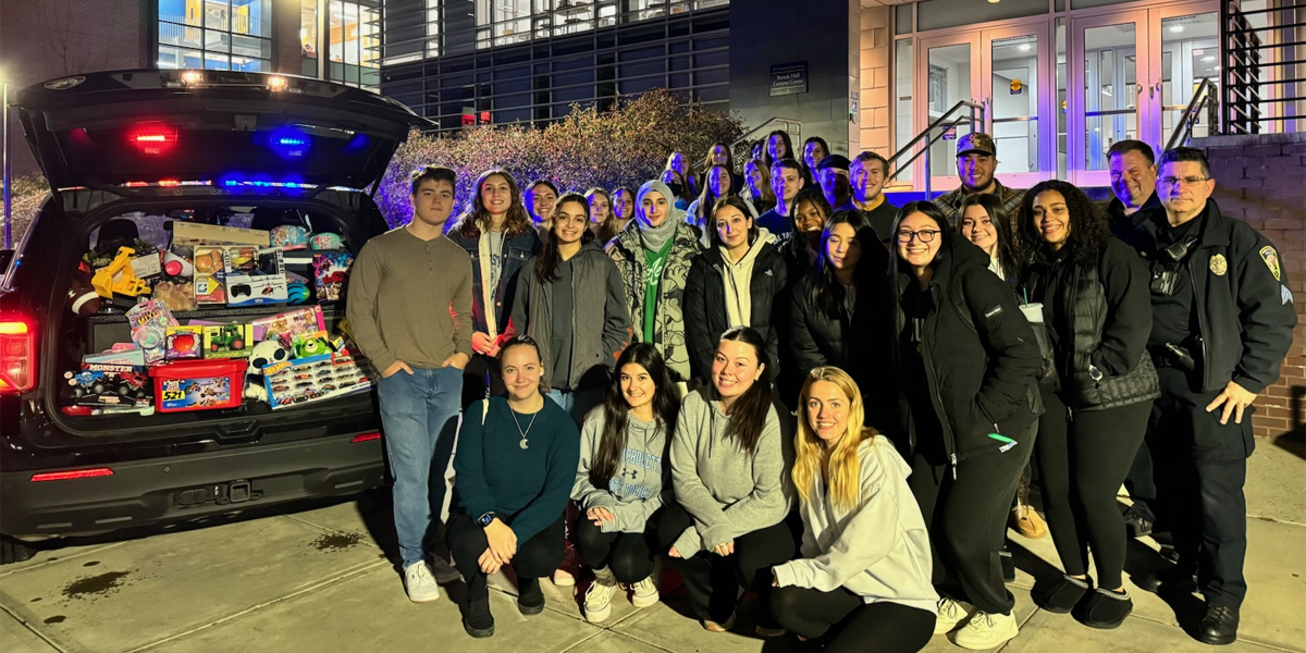 Students and officers standing near Bartels Campus Center with a trunk full of Christmas gifts for charity.